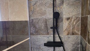 Een douche met een flexibele douchekop en bedieningseenheid bevestigd aan een stenen muur.