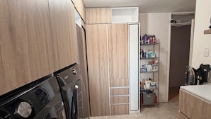 Ein Waschbereich mit Waschmaschine und Trockner, einem Stauraumschrank und einer Ablage mit Toilettenartikeln.