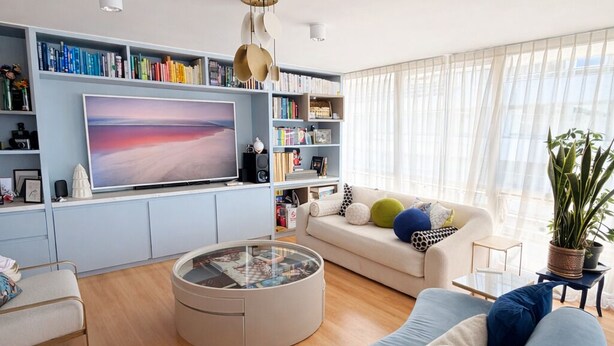 Ein modernes Wohnzimmer mit einem großen Flachbildfernseher, einem runden Couchtisch, einer Couch und einem Bücherregal voller Bücher.