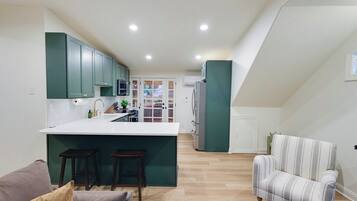 Une cuisine moderne avec des meubles de couleur turquoise, un plan de travail blanc et un îlot central doté de tabourets. Le salon est agrémenté d’un fauteuil à rayures et d’un canapé.