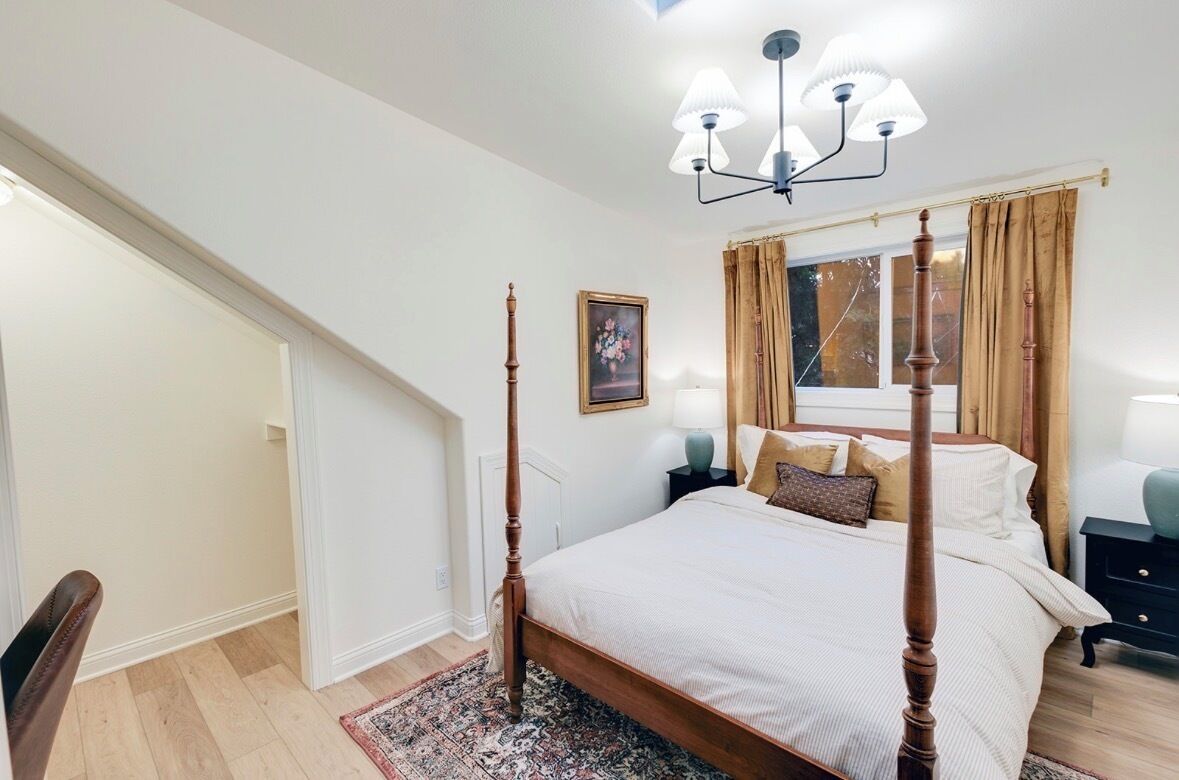 Une chambre à coucher avec un lit à baldaquin, un lustre, une table de chevet, une fenêtre avec des rideaux et une porte donnant sur une autre pièce.