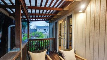 Une terrasse en bois avec deux fauteuils en osier et une table en bois, donnant sur un jardin et une maison.