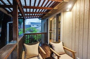 A wooden deck with two wicker chairs and a wooden table, overlooking a garden and a house. - Relax in this beautifully remodeled apartment that blends comfort and style. (Vancouver)