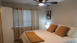 Ein Schlafzimmer mit einem Bett, einem Deckenventilator, einem Fenster mit Jalousien und einer Tür.