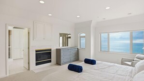 Een slaapkamer met een open haard, een groot raam met uitzicht op zee en een moderne dressoir.