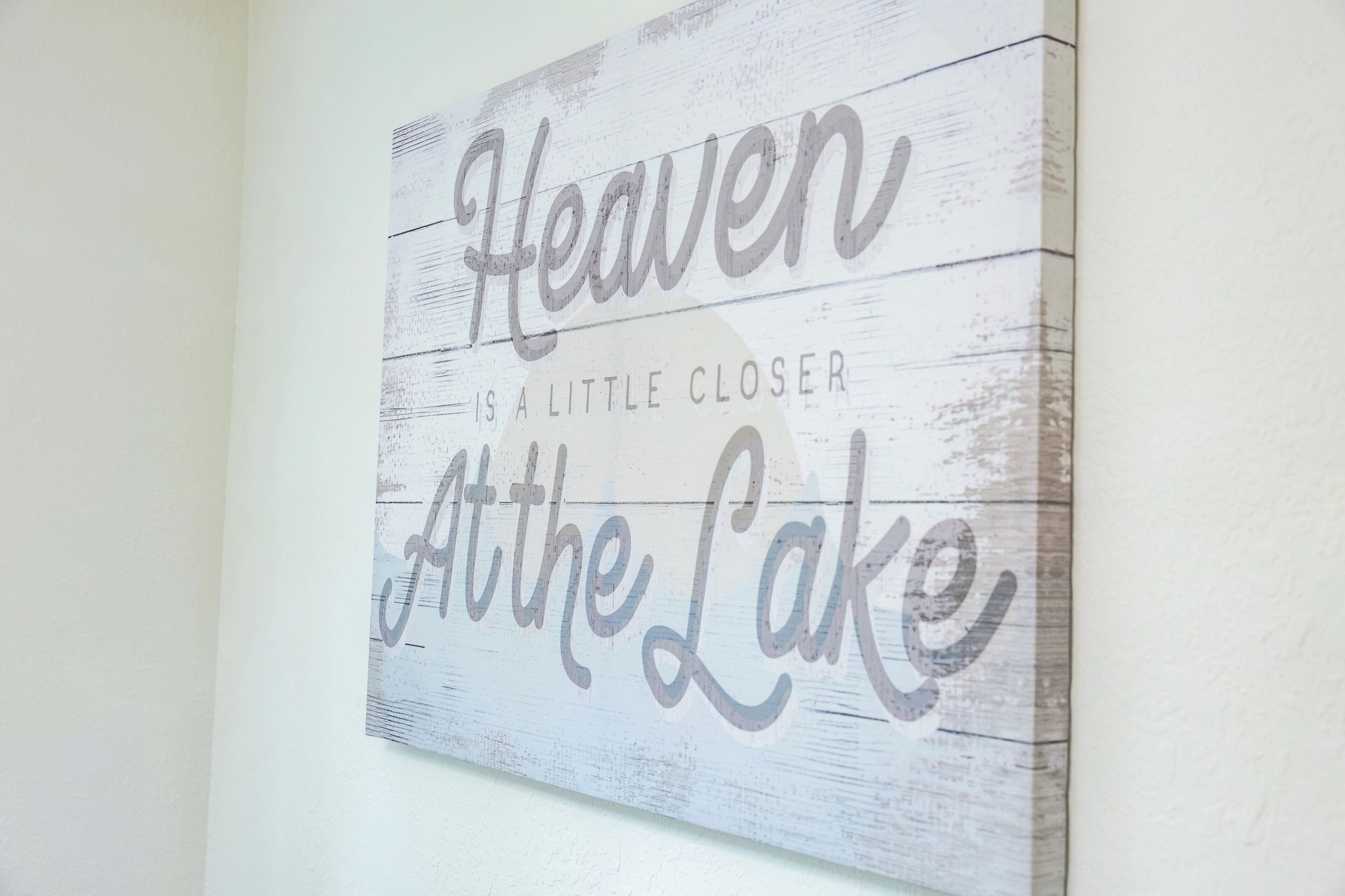 A wall with a wooden sign that reads 'Heaven is a little closer at the lake.'