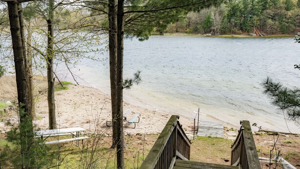 A wooden deck leading to a sandy beach by a calm lake, surrounded by trees.