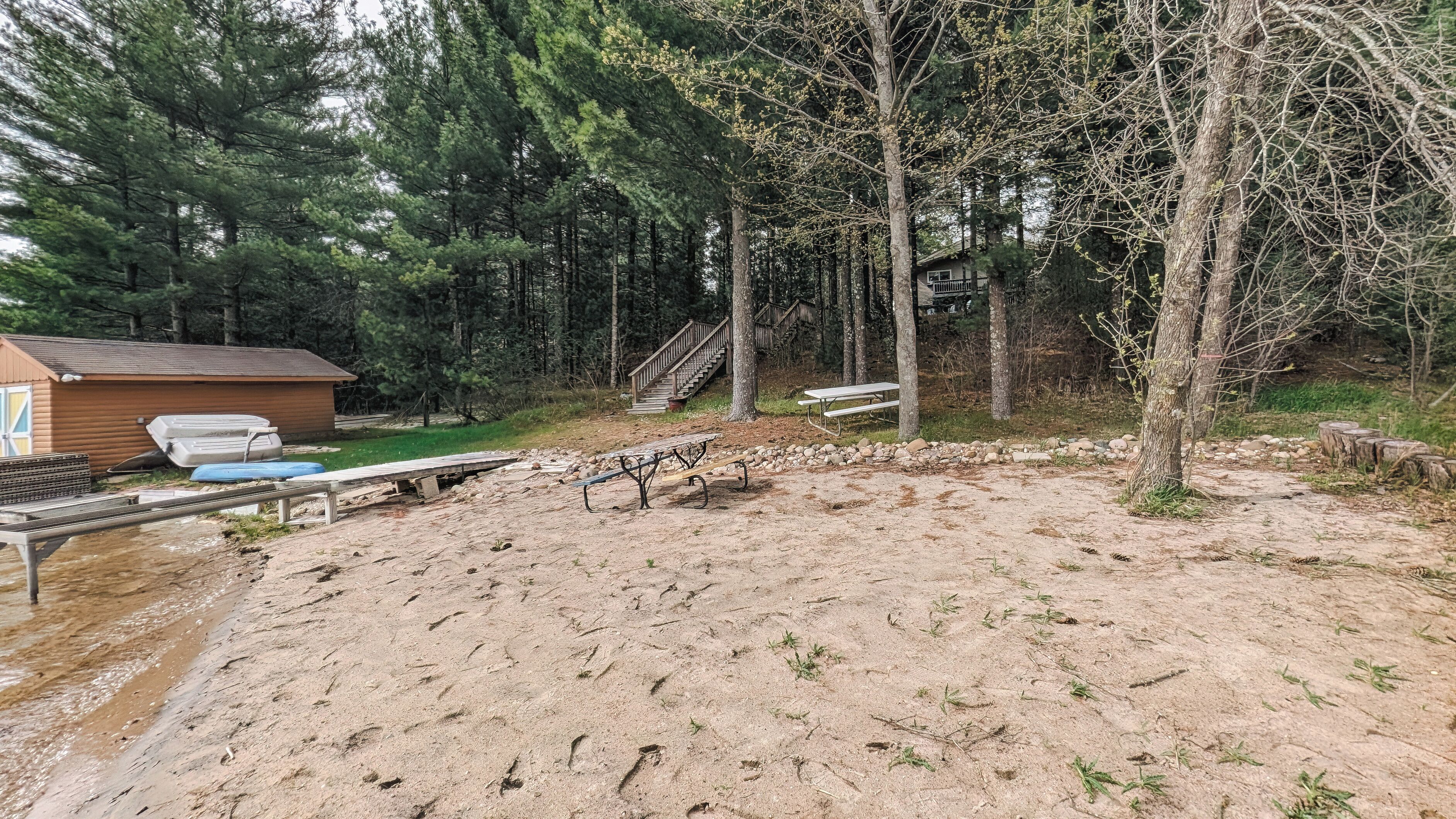 A sandy outdoor area with picnic tables, a small cabin, and a staircase leading into a forest.