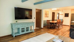 A living room with a flat-screen TV, a blue cabinet, a dining table with chairs, and a wooden floor.
