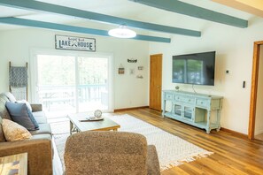 A living room with a couch, a coffee table, a TV, and a sign reading 'Lake House Established 2020'.