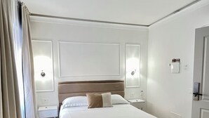 Hotellihuone, jossa on suuri sänky, kaksi yöpöytää, yölamppu, ovi ja ikkuna, jossa on verhot.