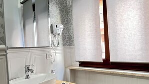 Kylpyhuoneessa on valkoinen pesuallas, allaskaappi ja peili. Seinällä on hiustenkuivaaja ja ovessa pyyhe.