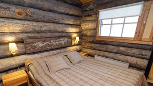 Un dormitorio tipo cabaña de troncos con una cama, dos lámparas de noche, una mesita de noche y una ventana con vistas a las montañas.