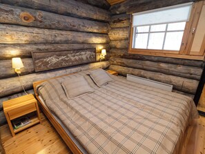 Ein Schlafzimmer in einer Blockhütte mit einem Bett, zwei Nachttischlampen, einem Nachttisch und einem Fenster mit Bergblick.