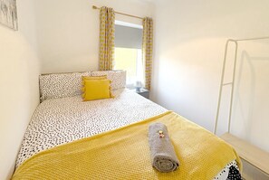 A neatly made bed with a polka dot and solid yellow bedspread, a rolled towel, and a yellow pillow. - Cottage with breathtaking views of the Rhondda Valley. (Trehafod)