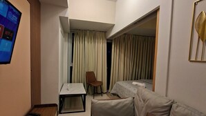 Une chambre d’hôtel moderne équipée d’un canapé, d’un petit bureau, d’une chaise, d’une télévision et d’un luminaire au plafond.
