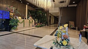 Un hall d’hôtel moderne avec un comptoir d’accueil en marbre, un grand luminaire suspendu et un espace d’accueil doté d’un écran numérique.