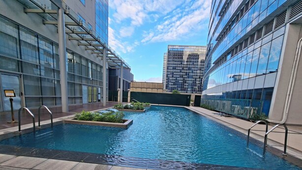 Un espace piscine intérieur moderne, avec une eau d’un bleu limpide, entouré de bâtiments en verre et de terrasses en bois.