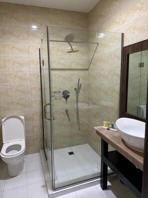 A glass-enclosed shower stall with a handheld showerhead and a wall-mounted faucet. - Vinpy Hotels (Uyo)
