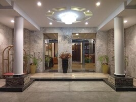 Un vestíbulo de hotel con suelo de mármol, grandes columnas y una escalera central.