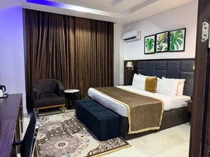 A bedroom with a bed, a chair, a small table, and a patterned rug. - Vinpy Hotels (Uyo)