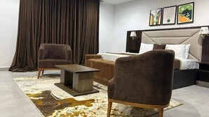 Une chambre d’hôtel moderne avec un grand lit, deux fauteuils, une petite table et une grande fenêtre avec des rideaux.