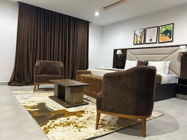Een moderne hotelkamer met een groot bed, twee fauteuils, een klein tafeltje en een groot raam met gordijnen.