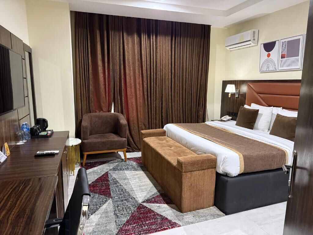 A hotel room with a bed, a desk, a chair, a sofa, and a large window with curtains.