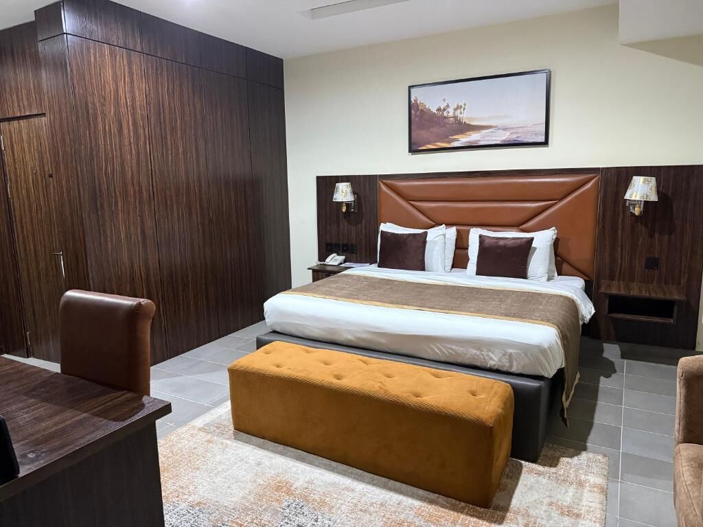 A hotel room with a large bed, a wooden wardrobe, a desk, and a bench.