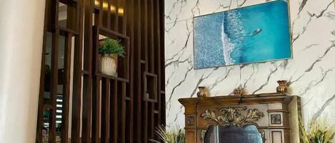 A lobby with a marble wall, a fireplace, and a large painting of a seascape.