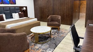 Une chambre d’hôtel moderne avec un grand lit, deux fauteuils, une table basse ronde et un mur d’accent en bois foncé.