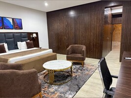 Una habitación de hotel moderna con una cama grande, dos sillones, una mesa de centro redonda y una pared decorativa de madera oscura.