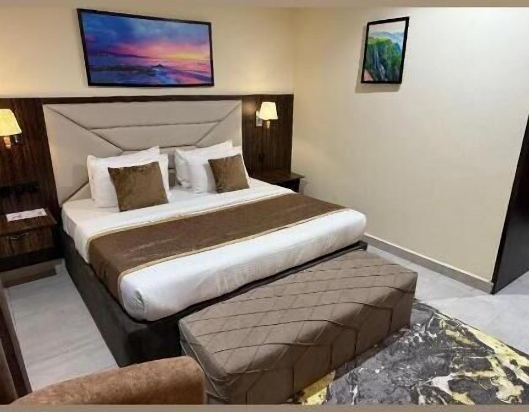 Ein Hotelzimmer mit einem großen Bett, zwei Nachttischen mit Lampen, einer Kopfteil und zwei an der Wand hängenden Bildern.