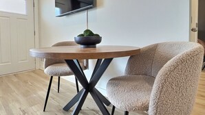 Et moderne spiseområde med et rundt bord, to komfortable stole, en sort skål med en plante og et vægmonteret fladskærms-tv.