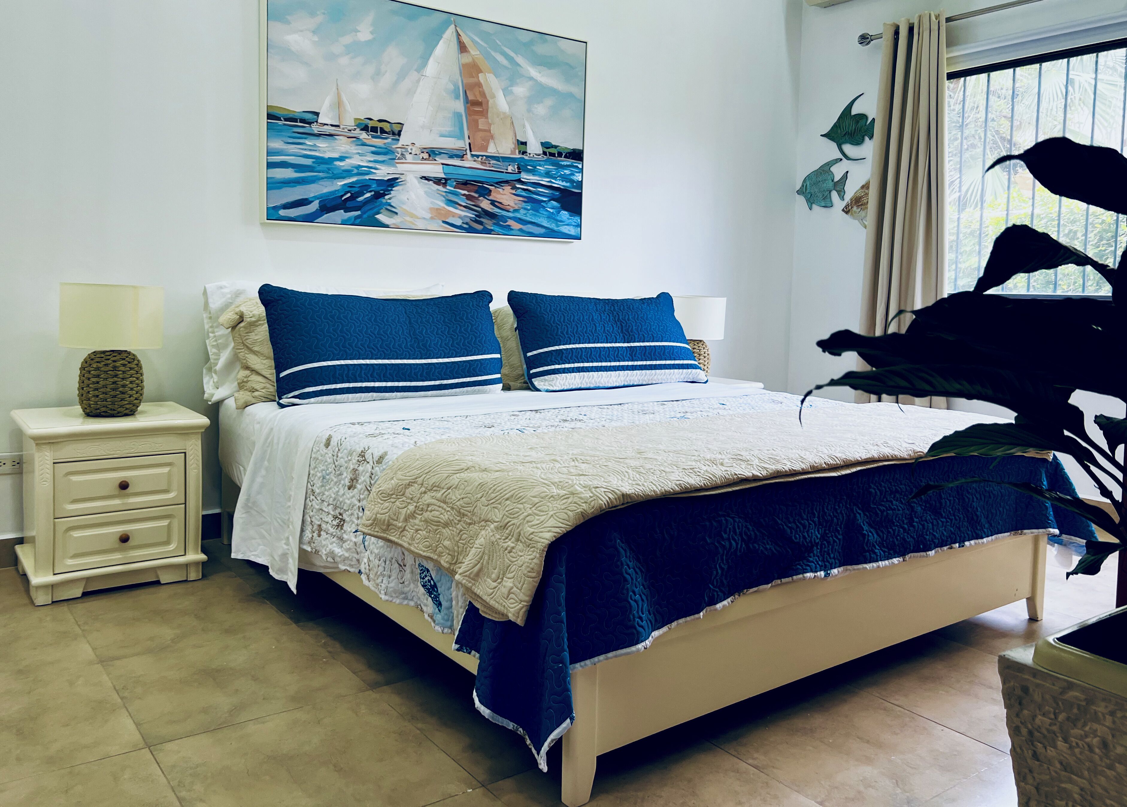 A bedroom with a bed, a nightstand, a lamp, and a painting of sailboats.