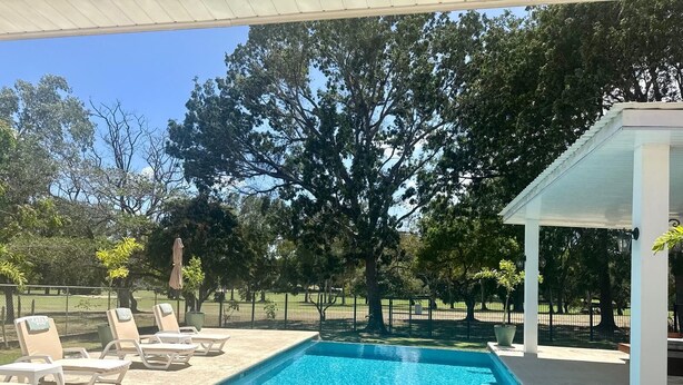 Ein rechteckiger Pool mit klarem, blauem Wasser, umgeben von Liegestühlen und einer überdachten Sitzgruppe.
