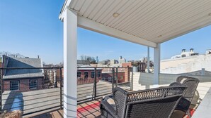 Een balkon met rieten meubels, een rood-wit gestreepte vloerkleed en een bloempot.