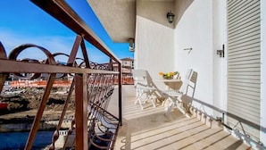 A balcony with a metal railing, white chairs, a small table with a fruit bowl, and a view of a construction site. - 1 bedroom stunning apartment in Podstrana (Podstrana)