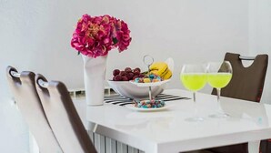 A dining table with a white vase of flowers, a bowl of fruit, a plate of macarons, and two glasses of yellow drink. - 1 bedroom stunning apartment in Podstrana (Podstrana)