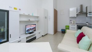 A modern living room with a flat-screen TV, white cabinetry, a sofa with cushions, and a kitchen area with cabinets and a microwave. - Gorgeous apartment in Brela with WiFi (Brela)