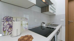 A kitchen with white tiles, a black stove, a sink, and a wooden door. - Gorgeous apartment in Brela with WiFi (Brela)