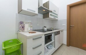 Une cuisine compacte avec des meubles blancs, un four encastré et un four à micro-ondes. On aperçoit un panier vert et un objet décoratif sur le plan de travail.