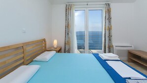 A hotel room with a bed, a nightstand with a lamp, a window with curtains, and a view of the sea. - Gorgeous apartment in Brela with WiFi (Brela)