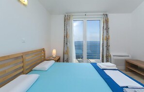 Une chambre d’hôtel avec un lit, une table de chevet avec une lampe, une fenêtre avec des rideaux et une vue sur la mer.