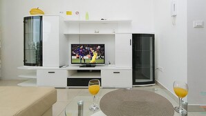 A modern living room with a flat-screen TV on a white entertainment unit, a glass coffee table, and two glasses of orange juice. - 2 bedroom awesome apartment in Brela (Brela)