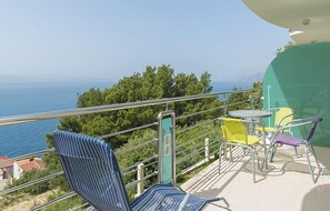 Ein Balkon mit Blick auf das Meer, ausgestattet mit gestreiften blauen Stühlen, einem gelben Stuhl und einem grünen Stuhl.