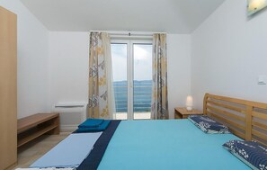 A bedroom with a bed, a bedside table, a lamp, a window with curtains, and a view of the sea. - Lovely apartment in Brela with WiFi (Brela)