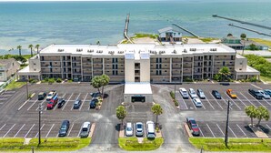 Um hotel com vários andares, um estacionamento em frente, vista para a praia e um píer que se estende na água.