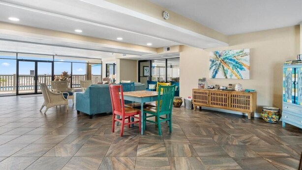 Um espaço interno amplo com mesa de jantar, cadeiras coloridas, um armário de madeira e uma janela grande com vista.