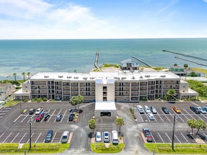 Ein mehrstöckiges Hotel mit Parkplatz vor der Tür, Blick auf den Strand und einer anlegenden Mole.
